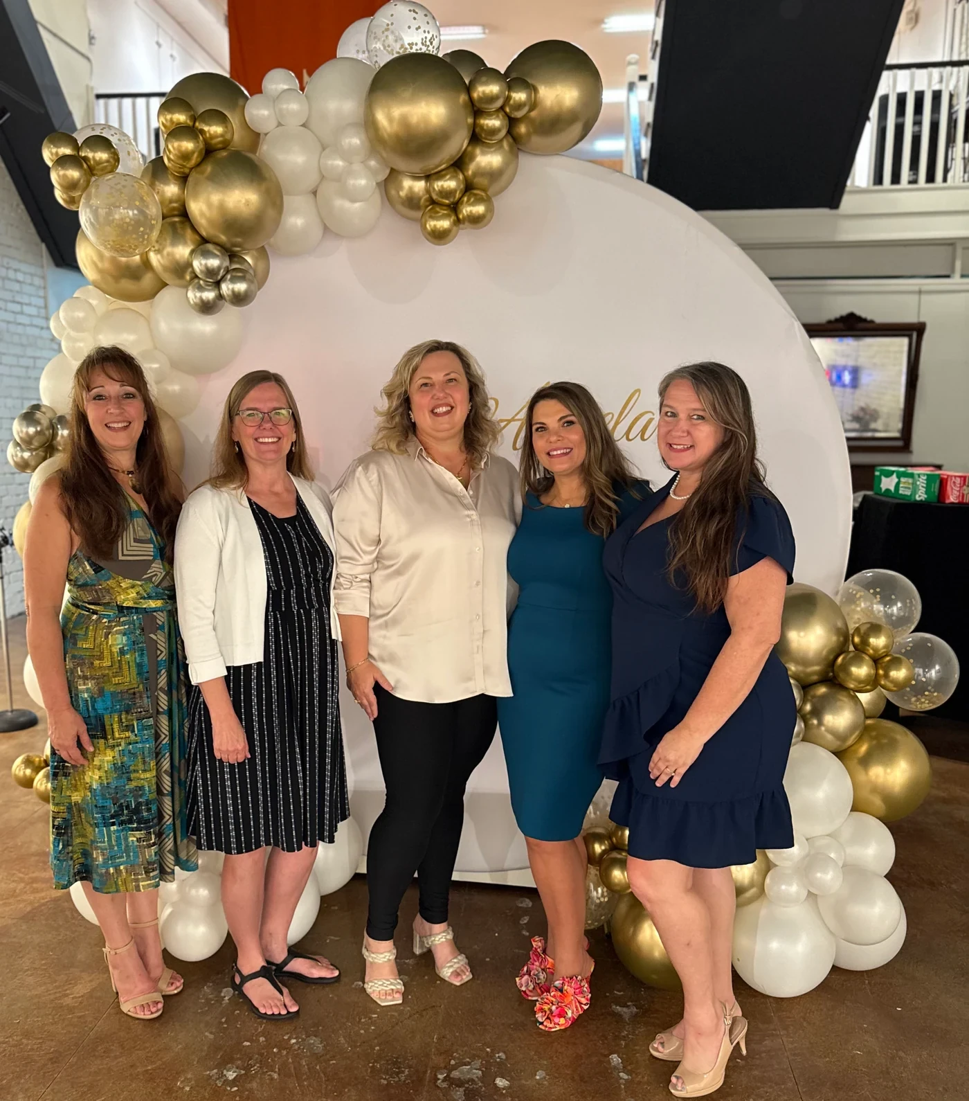 Five women smiling together at the birthday backdrop.