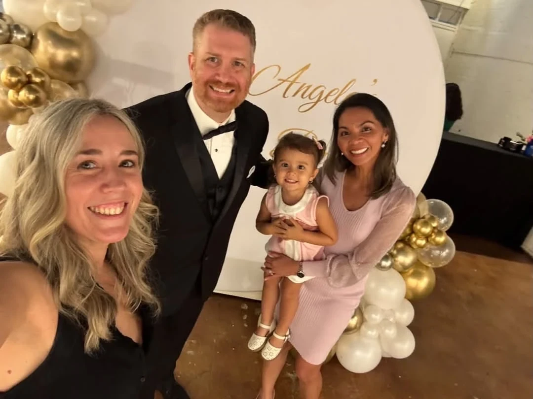 Three adults and a young child taking a selfie beside the birthday balloons.