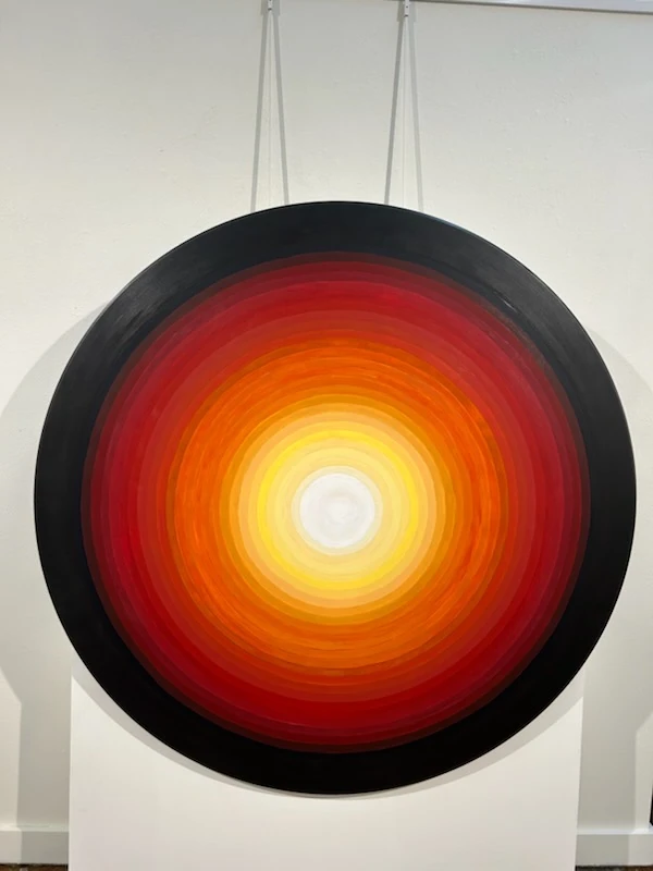 SUN GLOW, a circular painting with a white center and rings of yellow, orange, red and black.